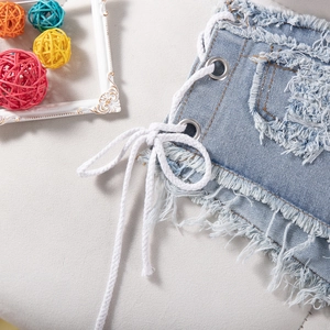 Dettaglio di pantaloncini in denim blu con allacciatura laterale, occhielli e orlo sfrangiato