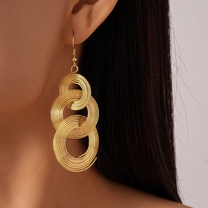 Macro detail of golden geometric tiered ring earrings on model showing spiral textures