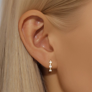 Macro shot of minimalist gold S925 silver hoop earrings with three inlaid white zircons