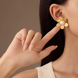 Polished gold flower earrings with pearl inlay worn by a model in a macro shot