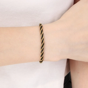 Detailed close-up of a black and 18K gold braided spiral bracelet on a wrist