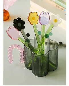 Macro shot of colorful glass flower spoons in a green textured glass mug on a desk