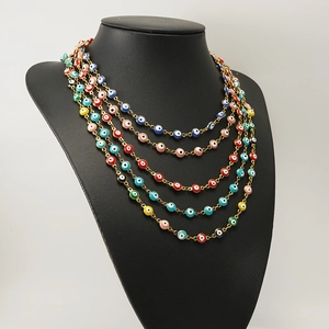 Detail of layered 18K gold stainless steel necklaces with colorful enamel evil eye beads
