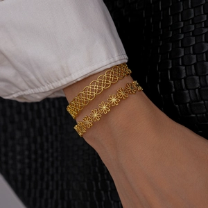 Close-up of golden hollow clover and daisy pattern open bangles on a wrist