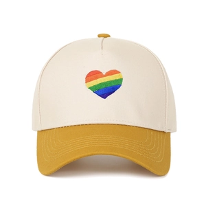 Dettaglio del ricamo cuore arcobaleno sulla visiera del cappello beige e giallo