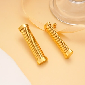 Macro detail of gold stainless steel column earrings with horizontal threaded texture