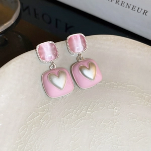 Macro detail of pink flower heart stud earrings on a textured ceramic plate backdrop