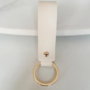 Detail of off-white leather keychain with gold metal ring on marble surface