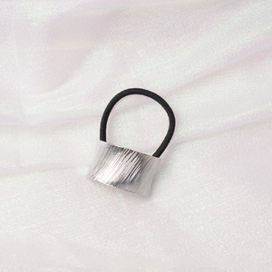 Close-up of a silver brushed metal hair ring with a black elastic band on white fabric
