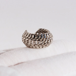 Silver chain woven ear cuff in metallic minimalist style on a white textured background