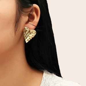 Détail d'une boucle d'oreille cœur dorée avec texture plissée sur un mannequin femme