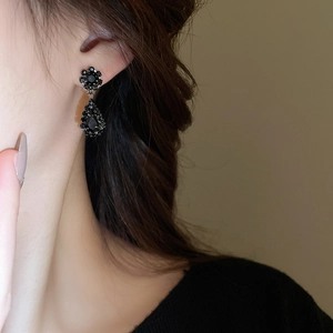 Detail of elegant black crystal teardrop flower earring worn by a model in warm light