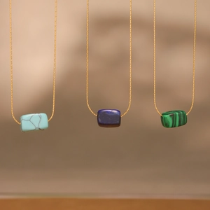 Three gold necklaces with blue lapis and green stone pendants in a minimalist style