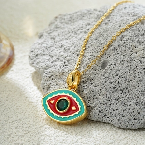 Detailed macro view of 18K gold evil eye pendant with red and green enamel and emerald gem