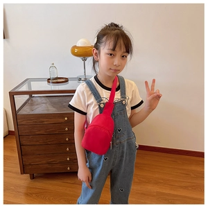 Kid's red fabric crossbody chest bag shown on model in a cozy indoor setting