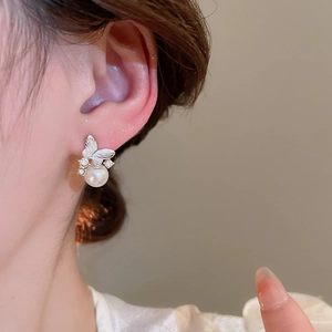 Close-up of a model wearing butterfly pearl earrings with white rhinestones and silver pins