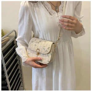 Detail of floral embroidery and metallic clasp on the cream straw saddle crossbody bag