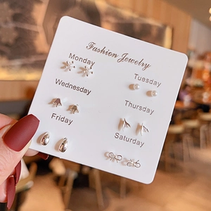 Close-up of 6 pairs of silver stud earrings featuring bows and pearls on a weekly card