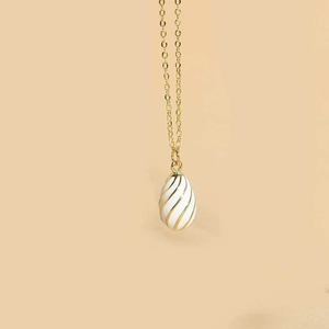 Detailed close-up of white enamel egg pendant with gold spiral patterns on a fine chain