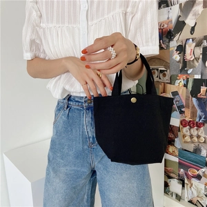 Detail of black canvas mini tote bag with gold snap button and stylish lifestyle accessories