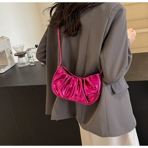 Fashion model wearing a metallic rose red pleated cloud bag in a modern indoor setting