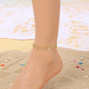 Close-up of gold fish tail anklet with green beads on a summer beach background