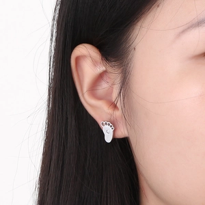 Close-up of minimalist silver paw print stud earring with zircon on model's ear