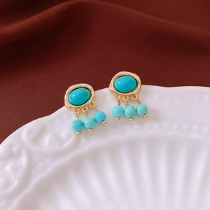 Detail of vintage gold earrings featuring turquoise stones on an embossed porcelain plate