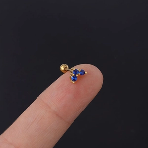 Macro shot of 20G gold stainless steel cartilage stud with blue cubic zirconia on fingertip