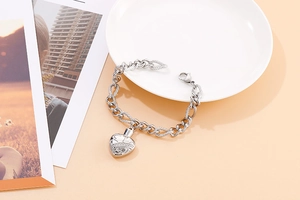 Detailed view of a polished silver heart charm on a chunky stainless steel link bracelet