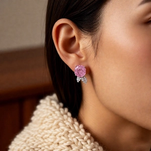 Close-up of pink rose earrings with silver zircon leaves worn by a model in soft light