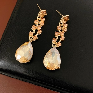 Macro detail of gold champagne pear-cut drop earrings on premium black leather surface
