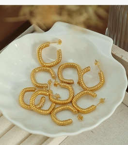 Detailed close-up of gold twisted rope hoop earrings resting on a white shell tray