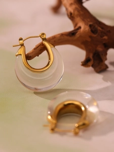 Close-up of U-shaped gold resin earrings displayed on a rustic wood piece with pastel background