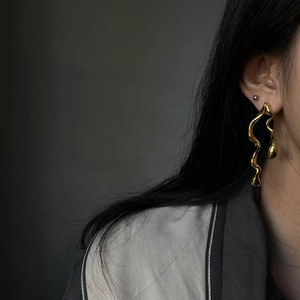 Detailed close-up of golden asymmetric snake earrings on model with liquid metal texture