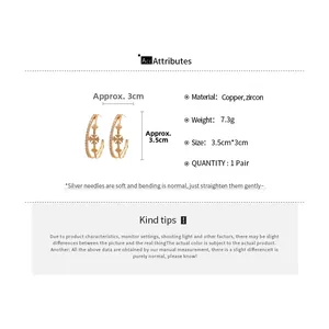 Détail de boucles d'oreilles doubles en forme de C dorées avec zircons et croix