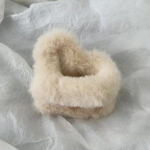Macro view of a heart-shaped plush hair claw clip in beige faux fur for elegant styling