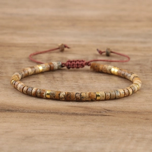 Detail of hand-woven emperor stone beaded bracelet with golden spacers and red cord