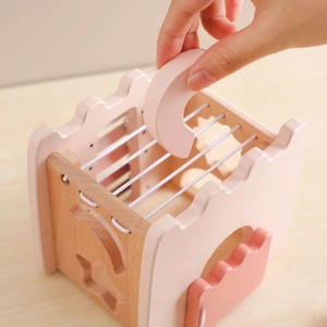 Close-up of wooden sensory toy showing hand placing pink block into elastic string box