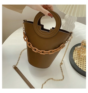Brown leather bucket bag with amber chain and round handle in a cozy lifestyle setting