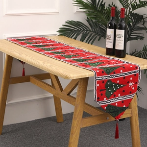 Detail of red knitted Christmas table runner with green trees, snowflakes and tassels