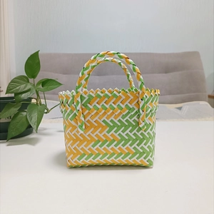 Close-up of a woven mini tote bag in green, yellow, and white plastic weave pattern