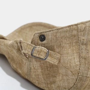 Close-up of adjustable metal buckle and strap on khaki linen-textured flat cap
