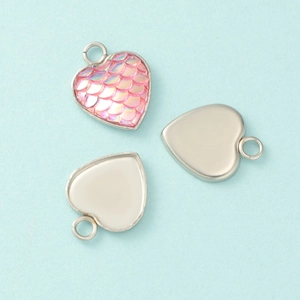 Macro detail of heart-shaped stainless steel pendant base and pink mermaid scale texture