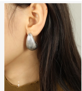 Detail of silver water-drop earring with wavy texture on a model’s ear