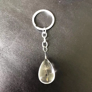 Dandelion seed keychain in teardrop resin pendant on a black matte surface