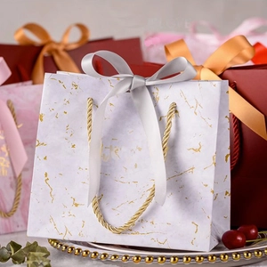 Detail of white marble pattern gift bag with golden rope handle and grey ribbon bow