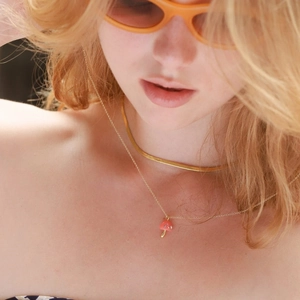 Close-up of pink enamel mushroom pendant with diamonds and golden snake chain layering