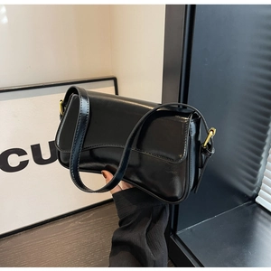 Detail of glossy black patent leather shoulder bag with sleek gold hardware accents