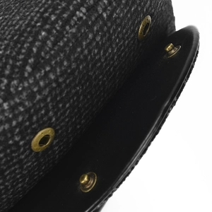 Detailed close-up of dark grey tweed fabric with black leather trim and bronze metal snap